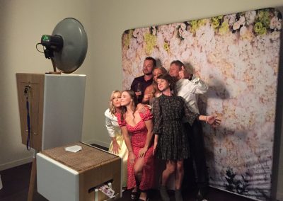 Group of people posing in front of a floral backdrop with a photo booth setup.