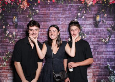 Three people standing in front of a brick wall with flower decorations and lanterns.