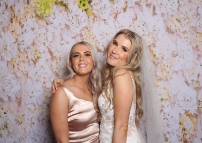 the bride and the bridesmaid posing against a floral backdrop.